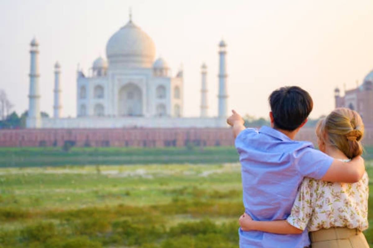 Couple viewing Taj Mahal from distance across green fields at sunset in Agra, India