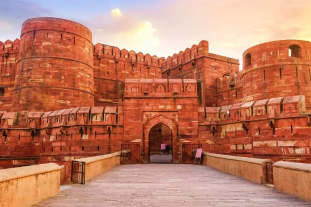 Red sandstone fortress with cylindrical towers and arched gateway at sunset, Agra Fort in India
