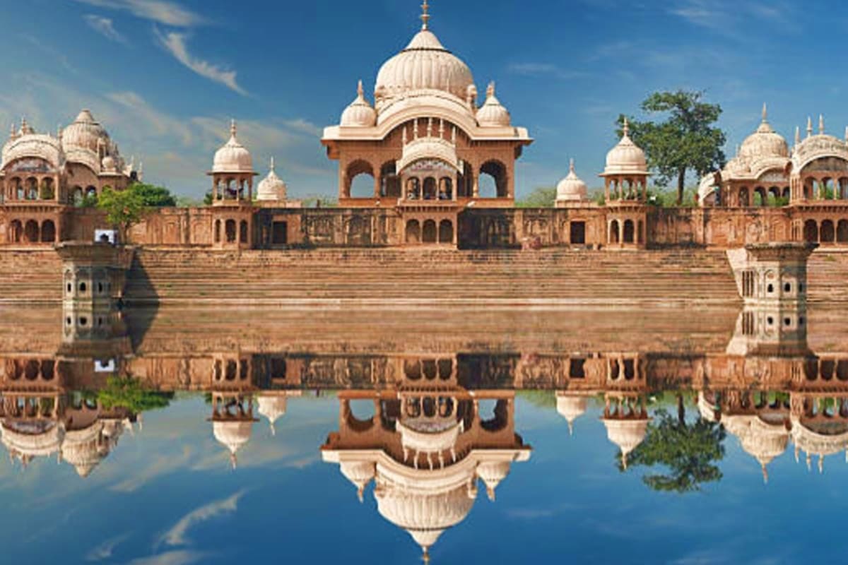Ornate cream and terracotta palace with domed architecture reflected in still water, featuring traditional Mughal and Indian 