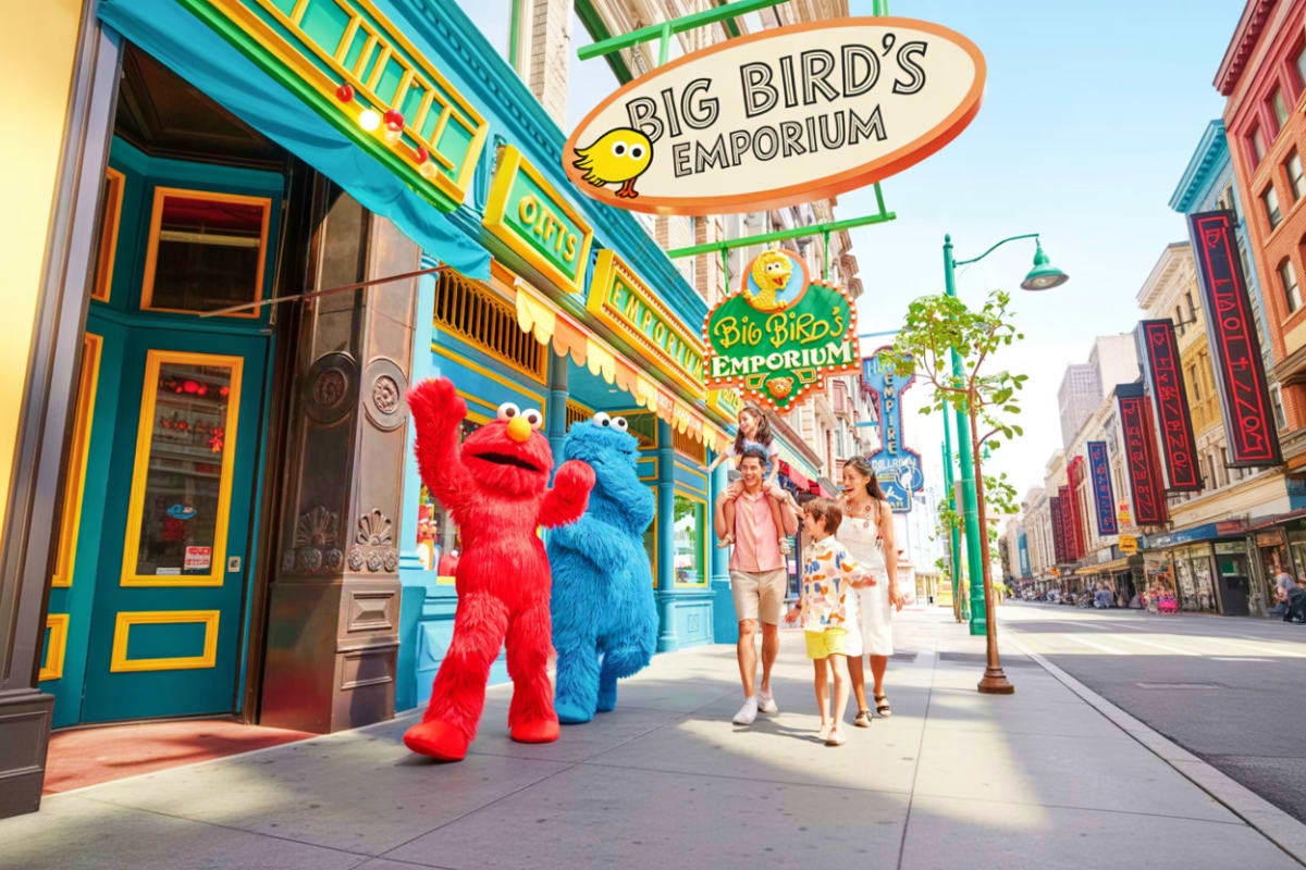 Elmo and Cookie Monster characters greeting family outside Big Bird's Emporium store on colorful street at Sesame Street them