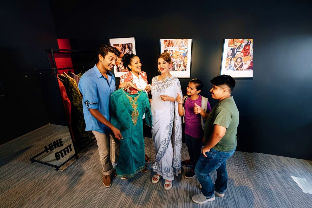 Family exploring cultural clothing display in museum with traditional garments and framed cultural artwork on dark walls