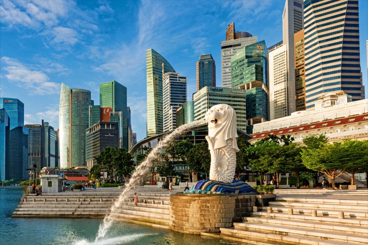 Merlion statue spouting water in Marina Bay with Singapore skyline of tall skyscrapers and waterfront promenade in background