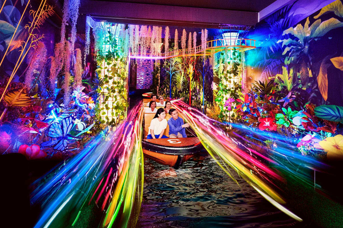 Luxury Sentosa Couple Getaway Couple riding illuminated boat through vibrant garden attraction with colorful neon lights and hanging tropical plants overhe