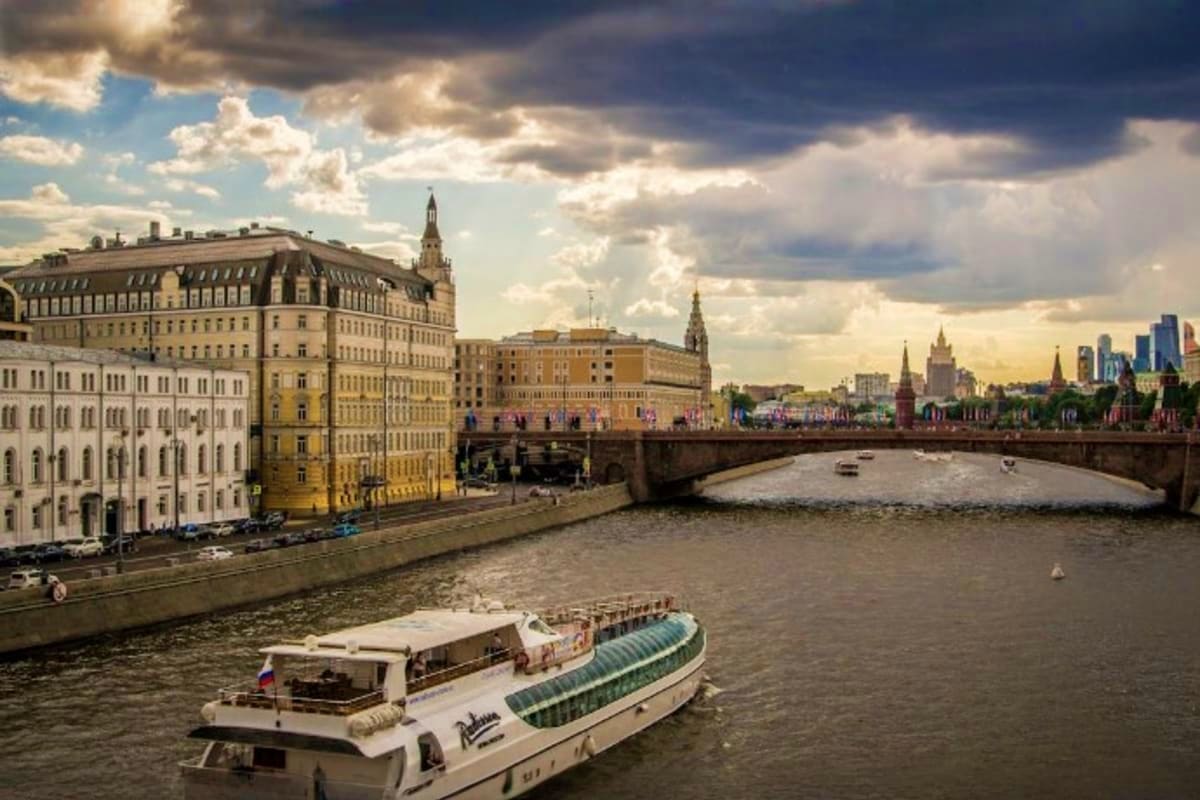 River cruise boats on Moscow River with Kremlin walls, historic buildings, and church spires in background under cloudy sky