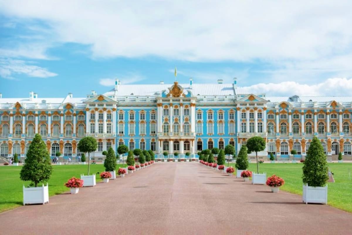 Catherine Palace in Pushkin, Russia with blue and gold baroque facade, manicured gardens, and tree-lined pathway leading to t