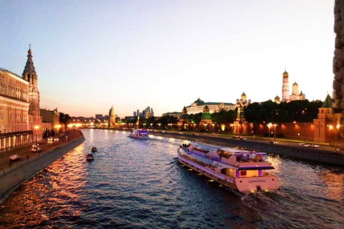 Evening river cruise boats on Moscow River with illuminated Kremlin walls, churches and golden domes at twilight
