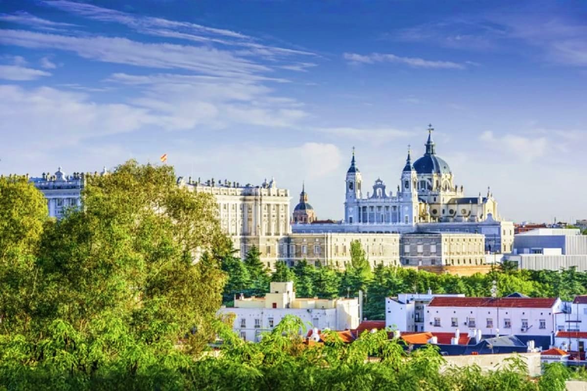 Royal Palace and Cathedral of Almudena with dome in Madrid skyline, surrounded by green trees and blue sky