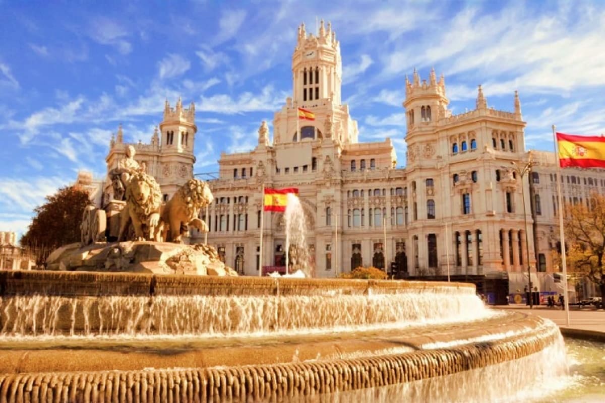 Plaza de Cibeles in Madrid with ornate fountain, neoclassical government buildings, and Spanish flags under blue sky