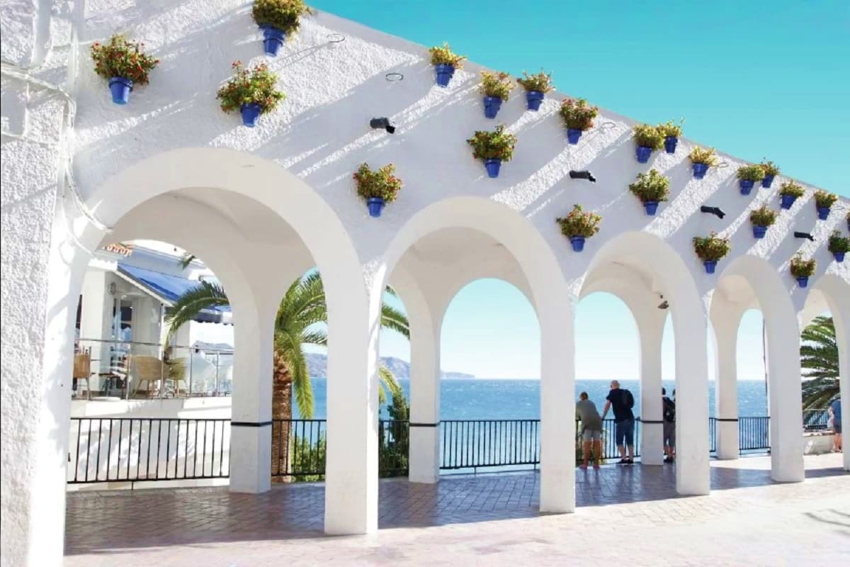 White arched colonnade overlooking Mediterranean Sea with hanging blue potted plants and palm trees at coastal resort