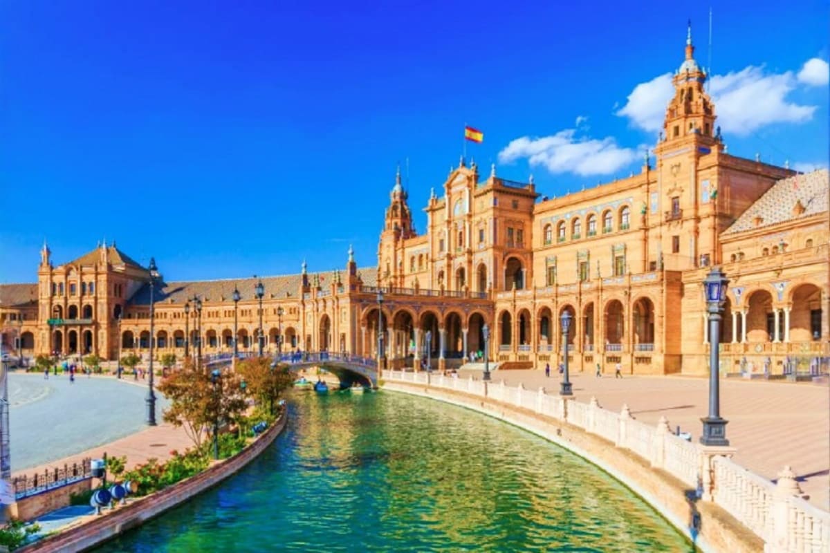 Plaza de España in Seville with ornate Renaissance buildings, canal, bridge, and Spanish flag under blue sky
