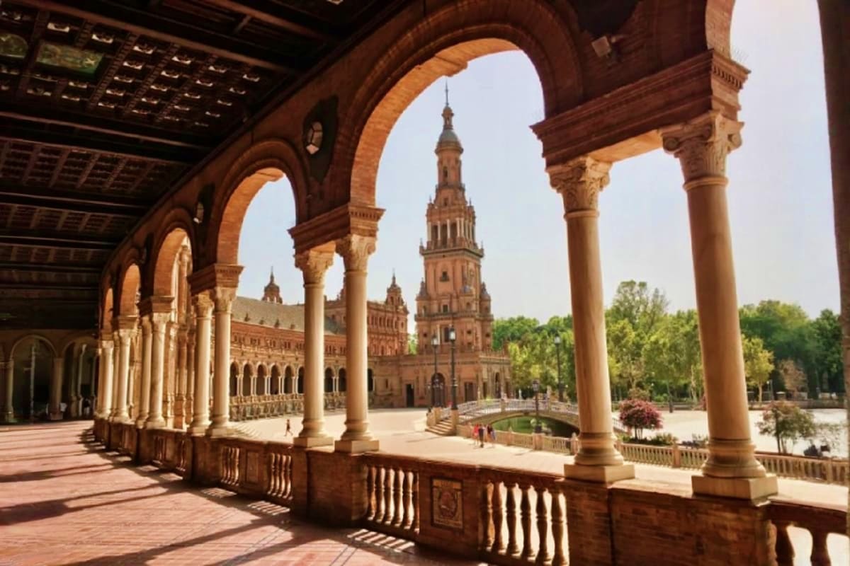 View through ornate arches of Plaza de España in Seville, Spain, showing Renaissance tower and brick architecture