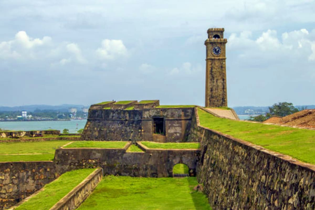 Historic stone fortress with grassy ramparts and clock tower overlooking coastal bay in Sri Lanka