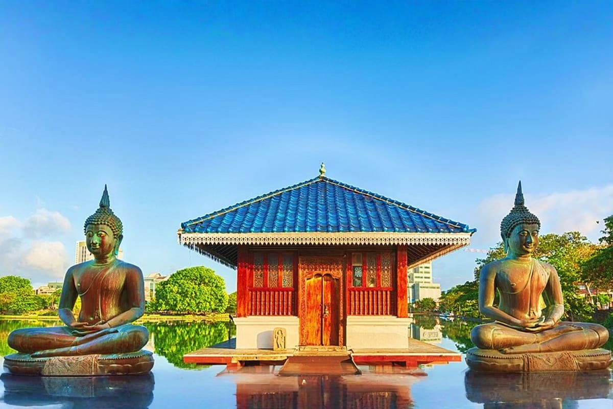 Buddhist temple with blue-tiled roof and red doors flanked by two bronze Buddha statues in meditation pose reflected in water