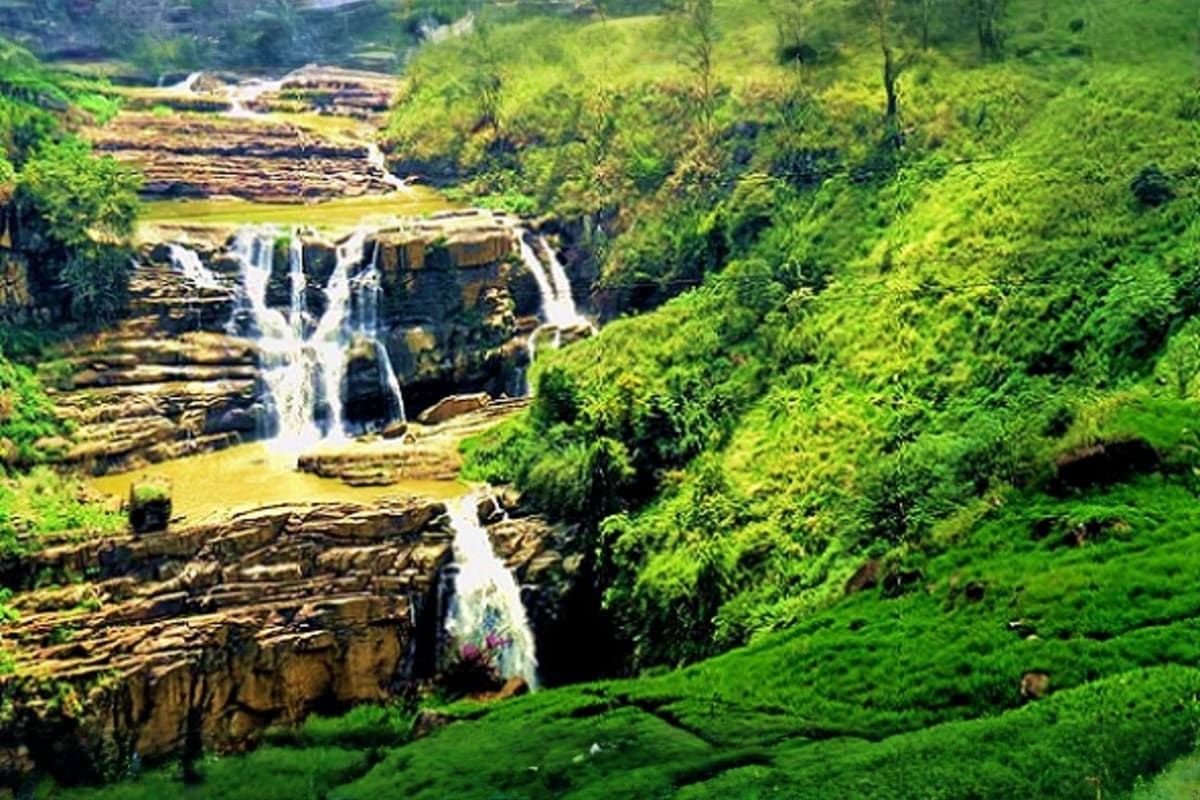Waterfall cascading down rocky cliffs surrounded by lush green forest and vegetation in Sri Lankan highlands