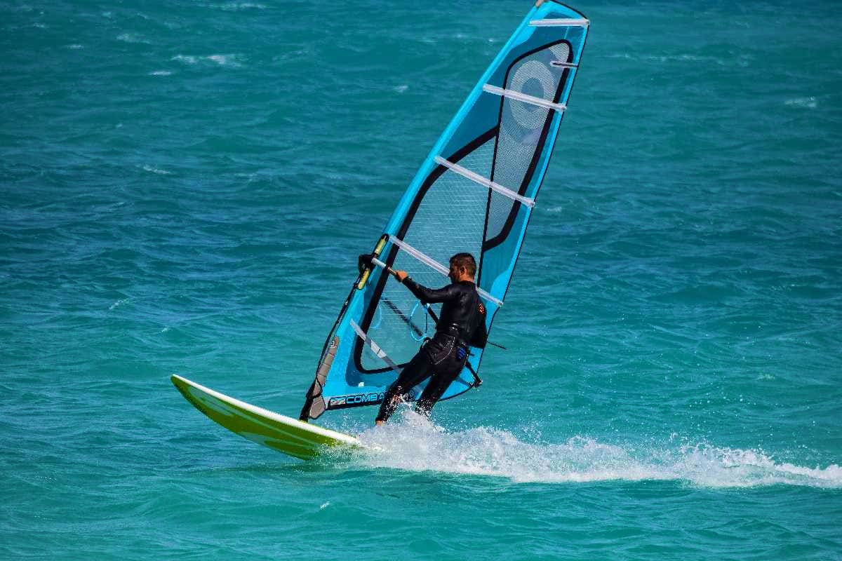 Windsurfer in wetsuit riding blue sail on turquoise ocean waves with white foam