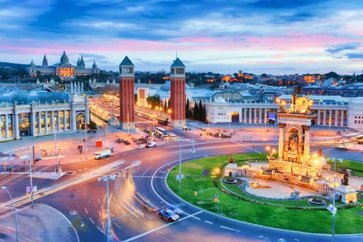 Barcelona's Plaça d'Espanya at dusk with twin brick towers, illuminated fountains, and historic buildings reflected in evenin