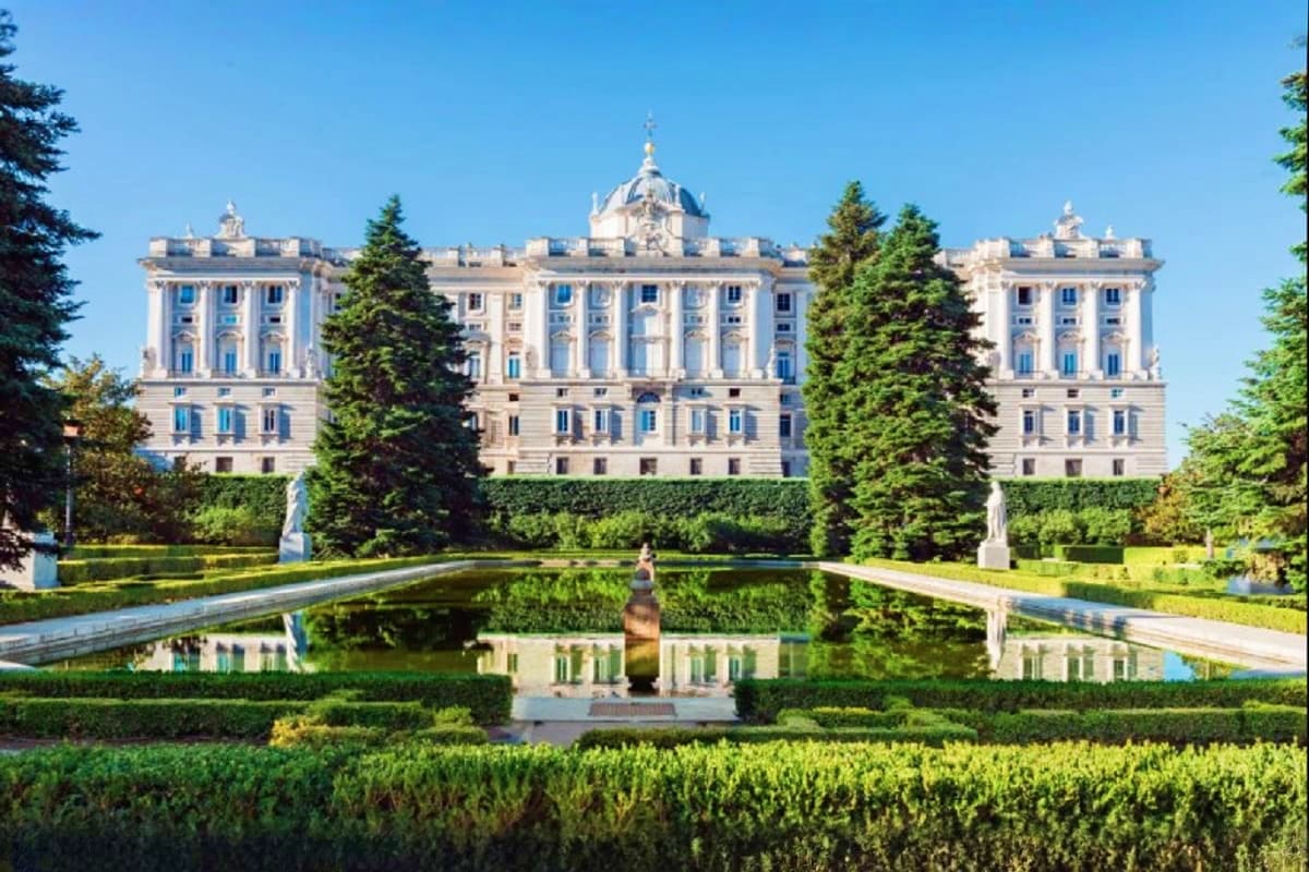 Royal Palace of La Granja de San Ildefonso reflected in formal garden pond with manicured hedges and evergreen trees