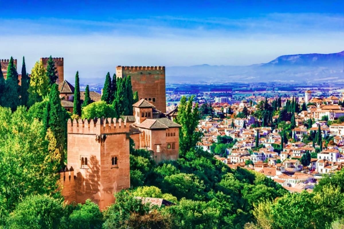 Alhambra palace fortress with red stone towers and cypress trees overlooking Granada cityscape and valley, Spain