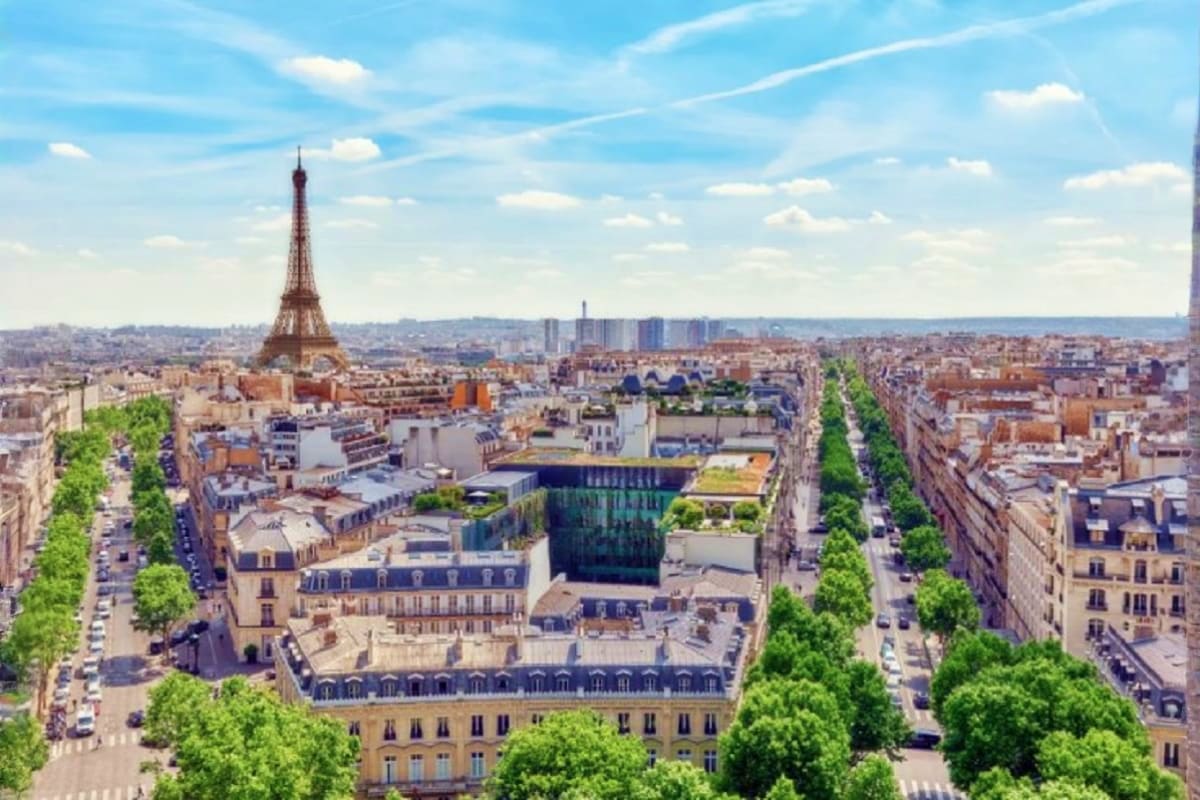 Aerial view of Paris cityscape with Eiffel Tower, tree-lined boulevards, and classical Haussmann buildings under blue sky