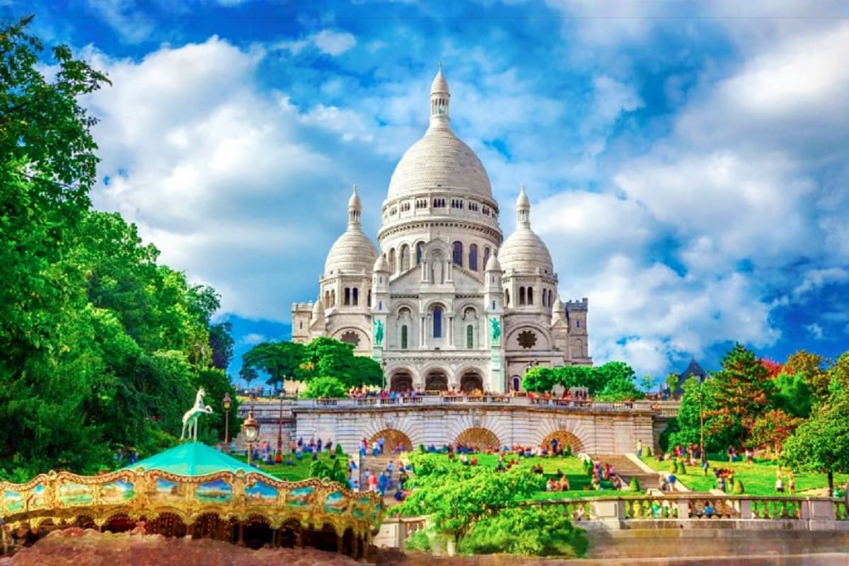 Sacré-Cœur Basilica in Montmartre, Paris with white dome, surrounding green trees, tourists on plaza, and blue sky with cloud