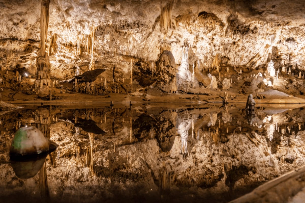 Underground cave chamber with limestone stalactites and stalagmites reflected in still water pool