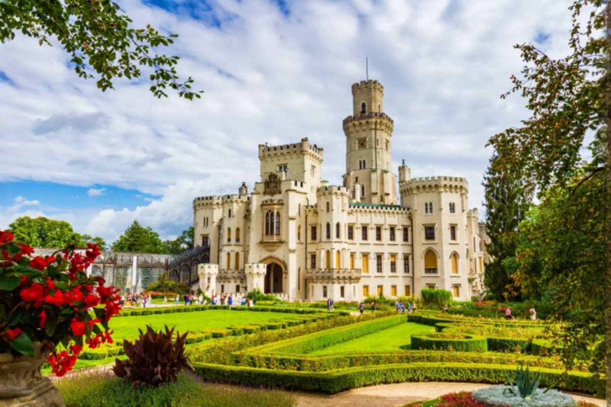 Neuschwanstein Castle surrounded by manicured gardens with red flowers, green hedges, and visitors on the grounds under a clo