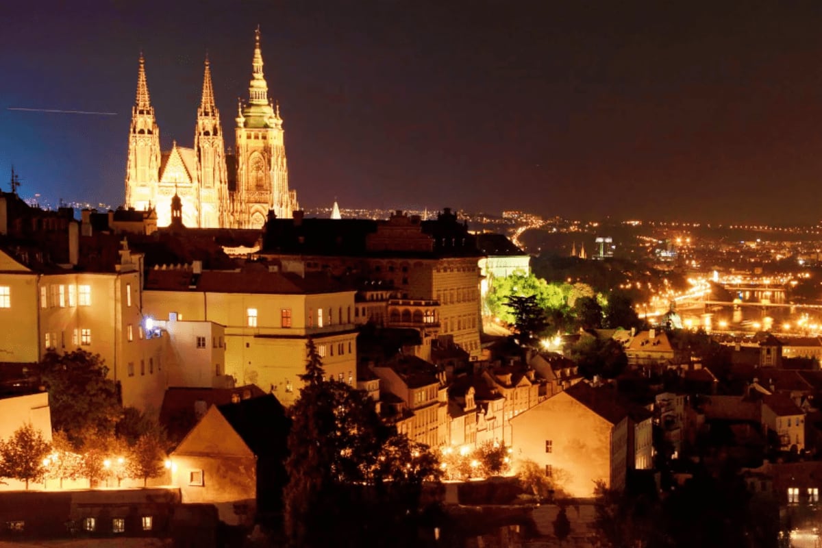 St. Vitus Cathedral illuminated at night overlooking Prague's old town with historic buildings and cityscape