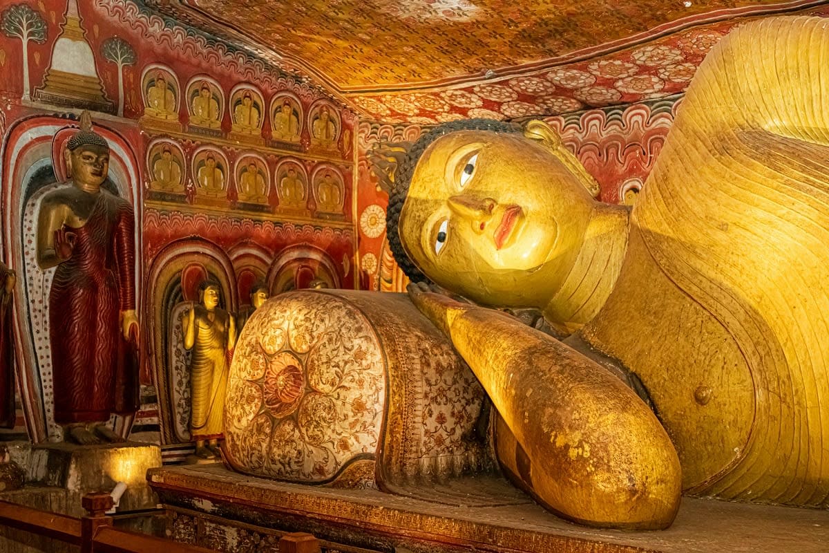 Reclining Buddha statue with gold leaf in ornate red temple with smaller Buddha figures and decorative wall panels