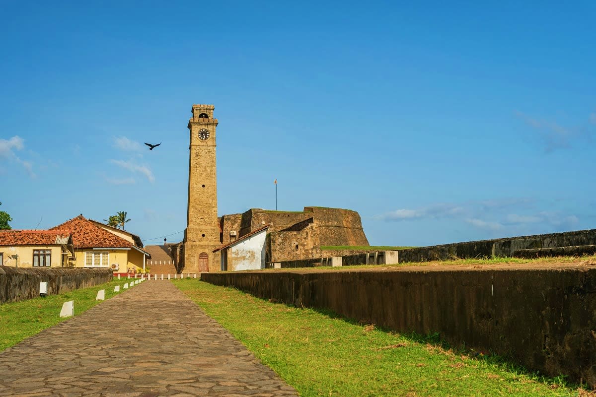 Historic lighthouse tower with clock face at Fort Galle, Sri Lanka, surrounded by colonial stone fortifications and pathways
