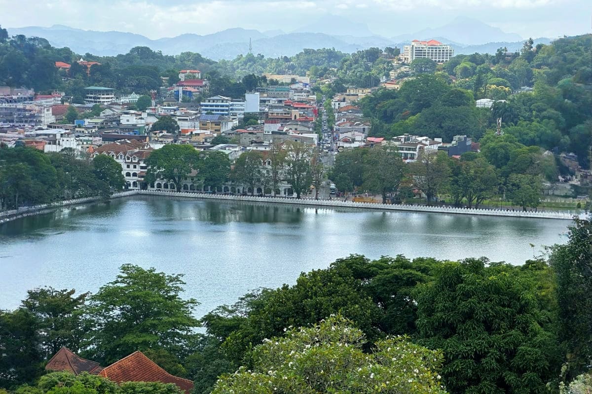 Scenic view of Kandy Lake with white balustraded embankment, colonial architecture, and lush green hills surrounding the hist