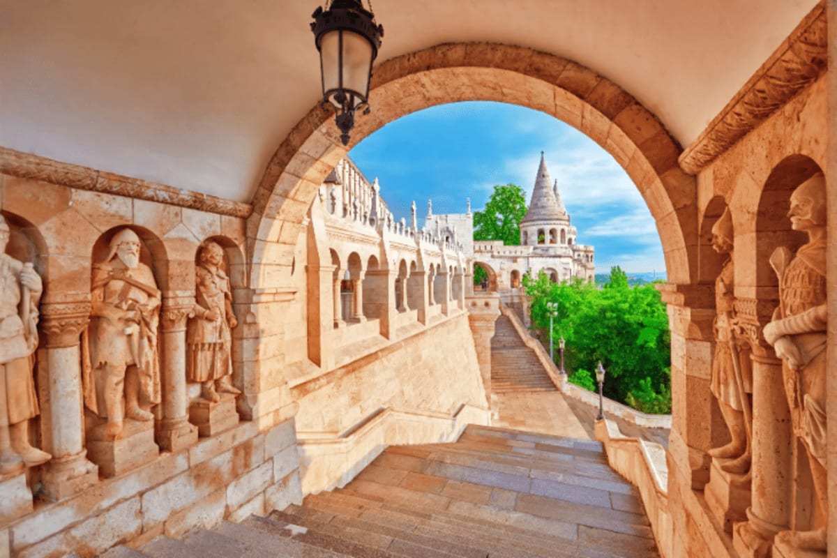 Stone archway with carved figures framing view of Fisherman's Bastion castle towers in Budapest with blue sky