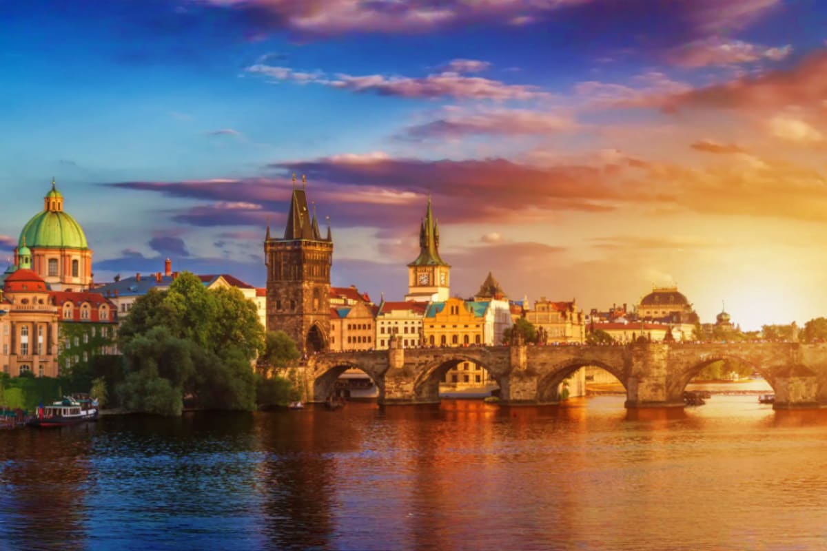 Charles Bridge and Prague skyline at sunset with Vltava River, historic towers and church spires illuminated in golden light