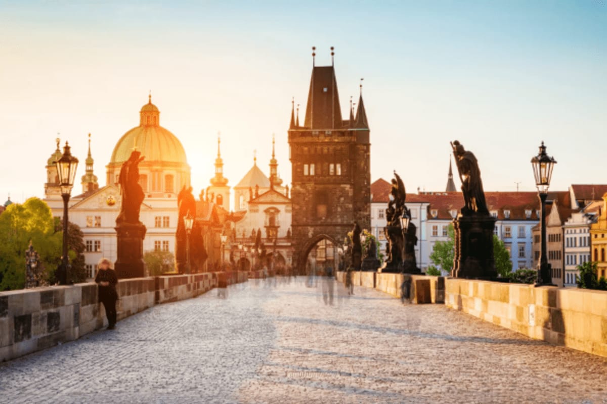 Charles Bridge at sunrise with statues, Gothic tower, and Prague cityscape including Church of Our Lady before Tyn in backgro