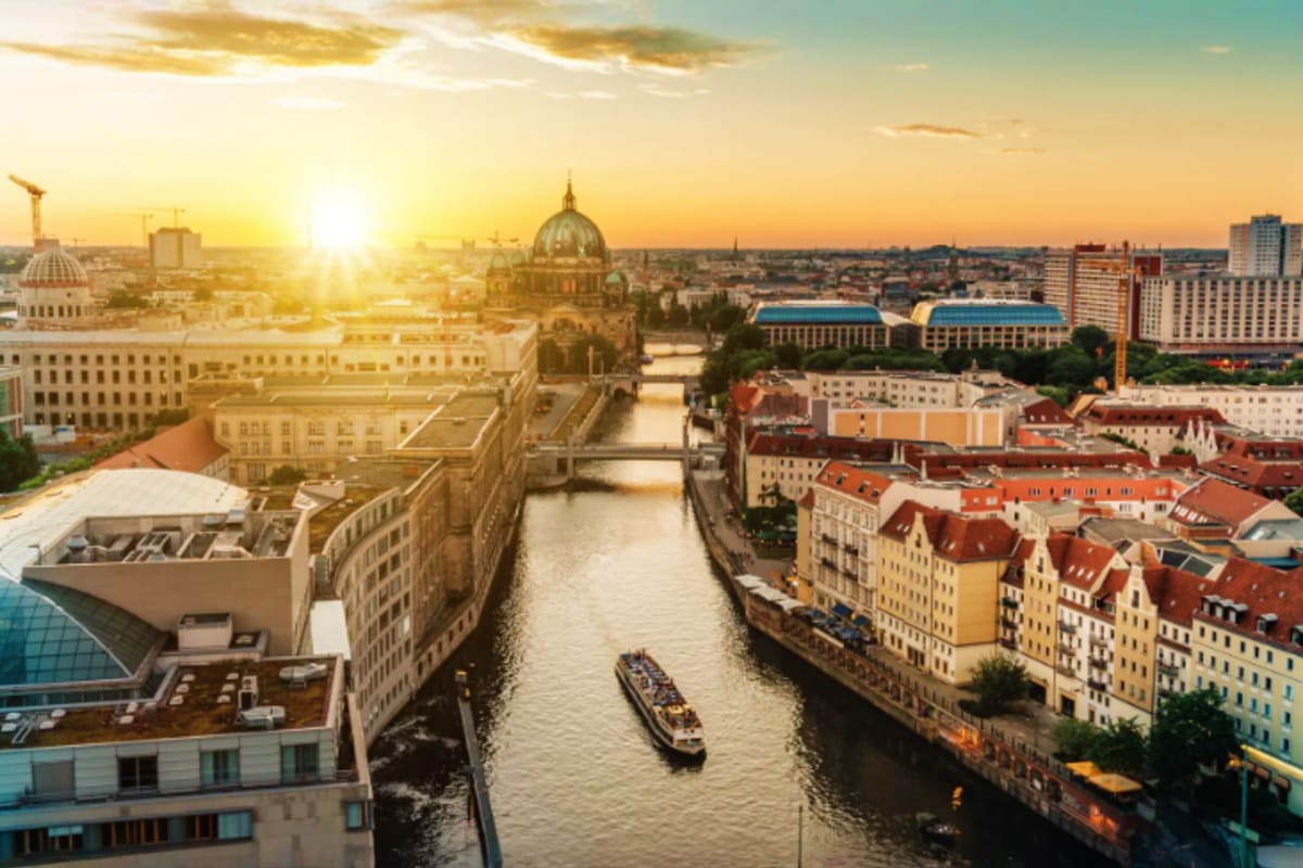 Sunset view of Berlin cityscape with Spree River, tour boat, and Berlin Cathedral dome visible along the waterfront