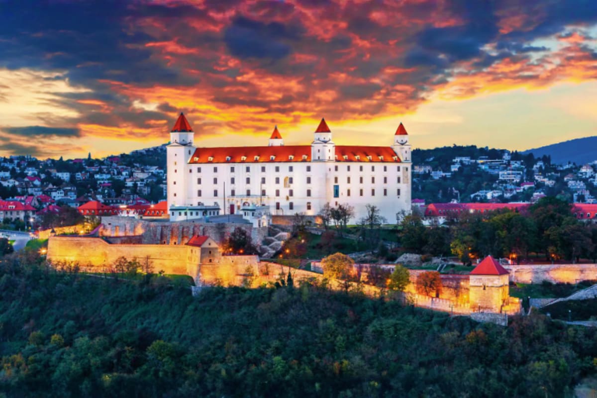 Bratislava Castle illuminated at sunset with red roofs and forested hills, Slovak landmark for European travel