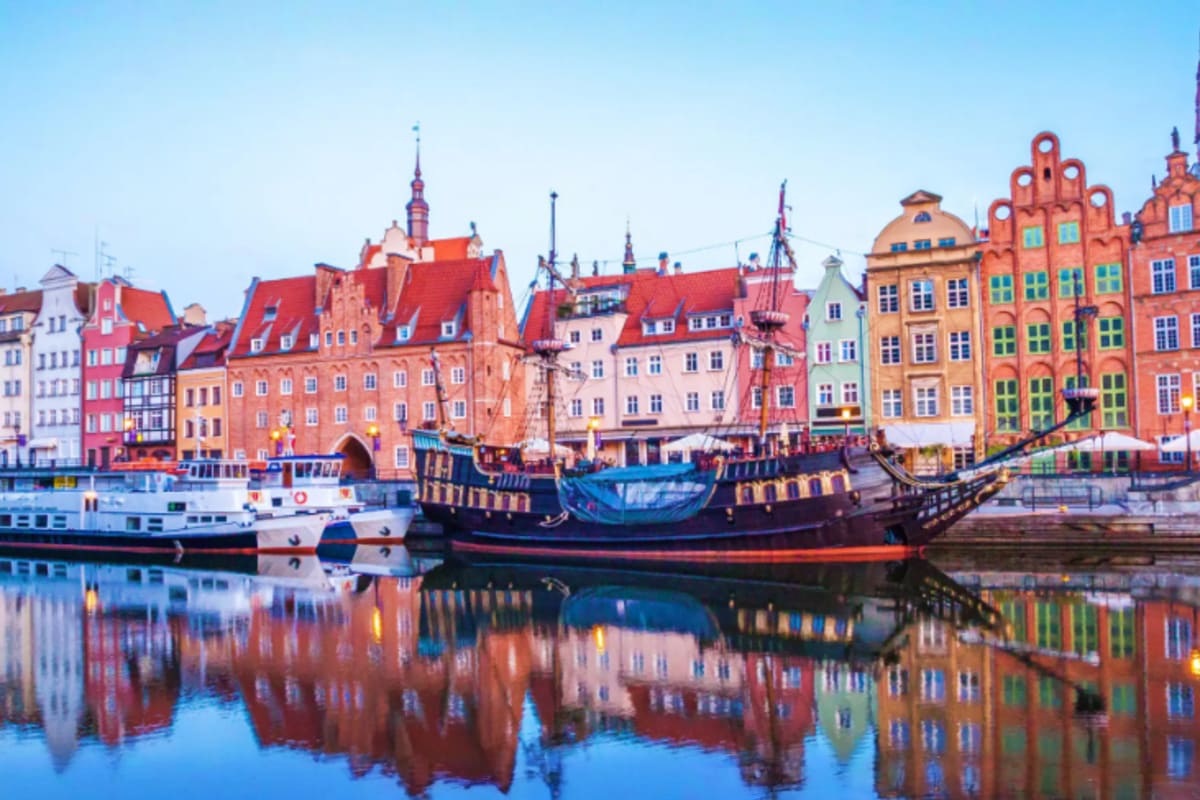 Colorful medieval buildings and historic ships reflected in calm water at Gdansk harbor, Poland