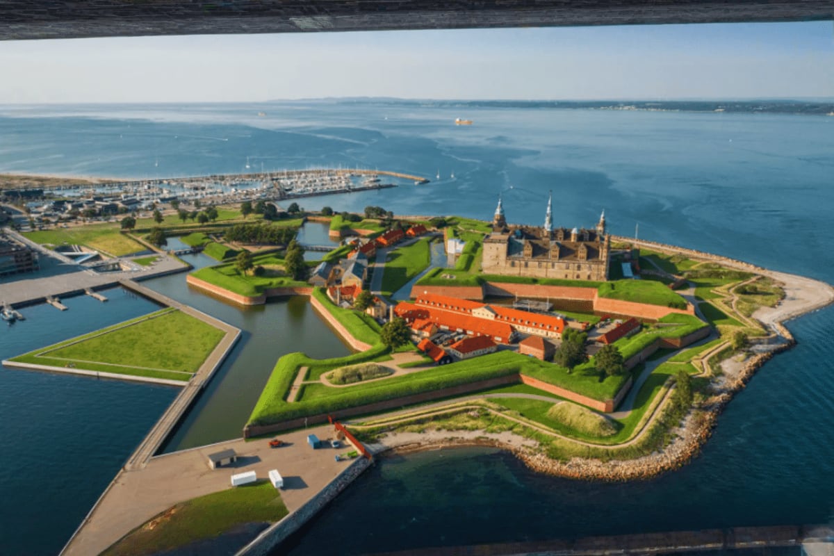 Aerial view of Kronborg Castle on island surrounded by moat with sailboats in Danish harbor and coastal town in background