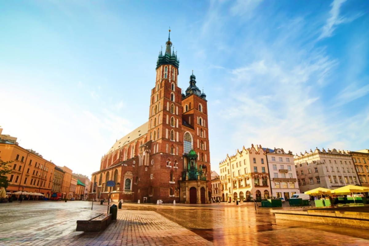 St. Mary Basilica in Krakow's Main Market Square reflecting on wet pavement under blue sky
