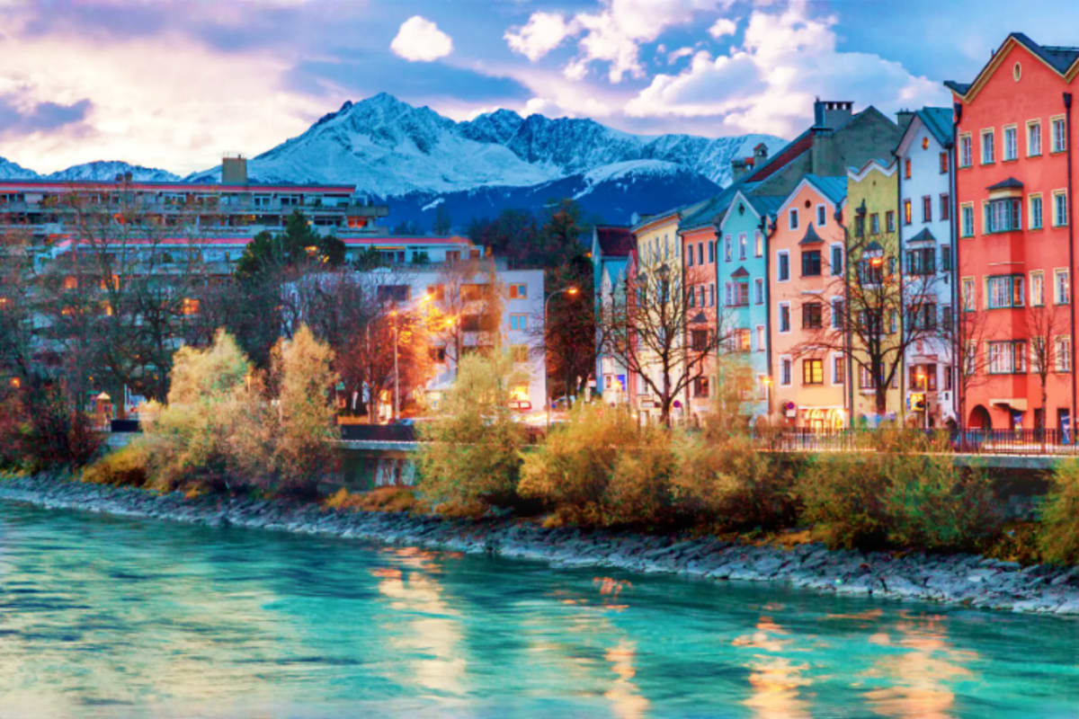 Colorful riverside buildings and snow-capped Alpine mountains at dusk in Innsbruck, Austria