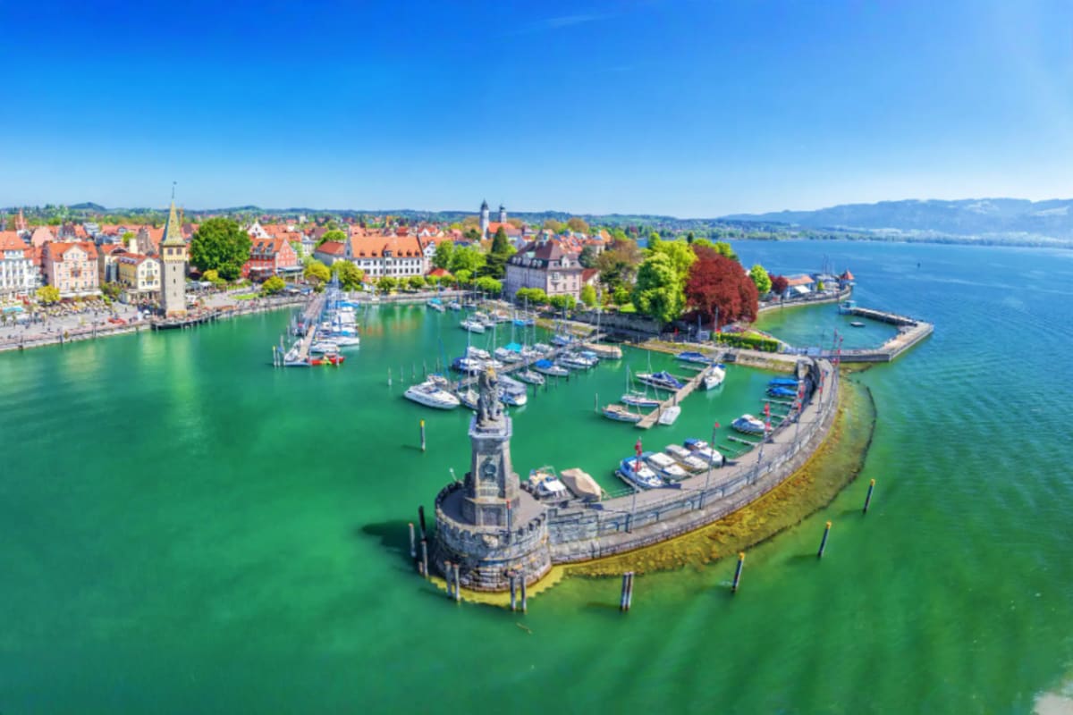 Aerial view of Lindau harbor with stone lighthouse, moored boats, and Alpine town architecture on Lake Constance