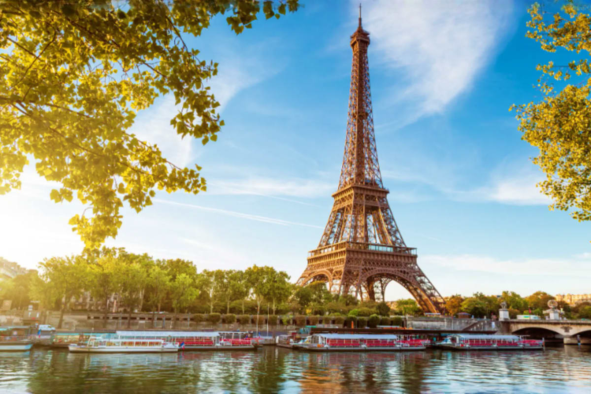 Eiffel Tower in Paris with Seine river and tourist boat in autumn, golden trees framing the iconic iron landmark under blue s