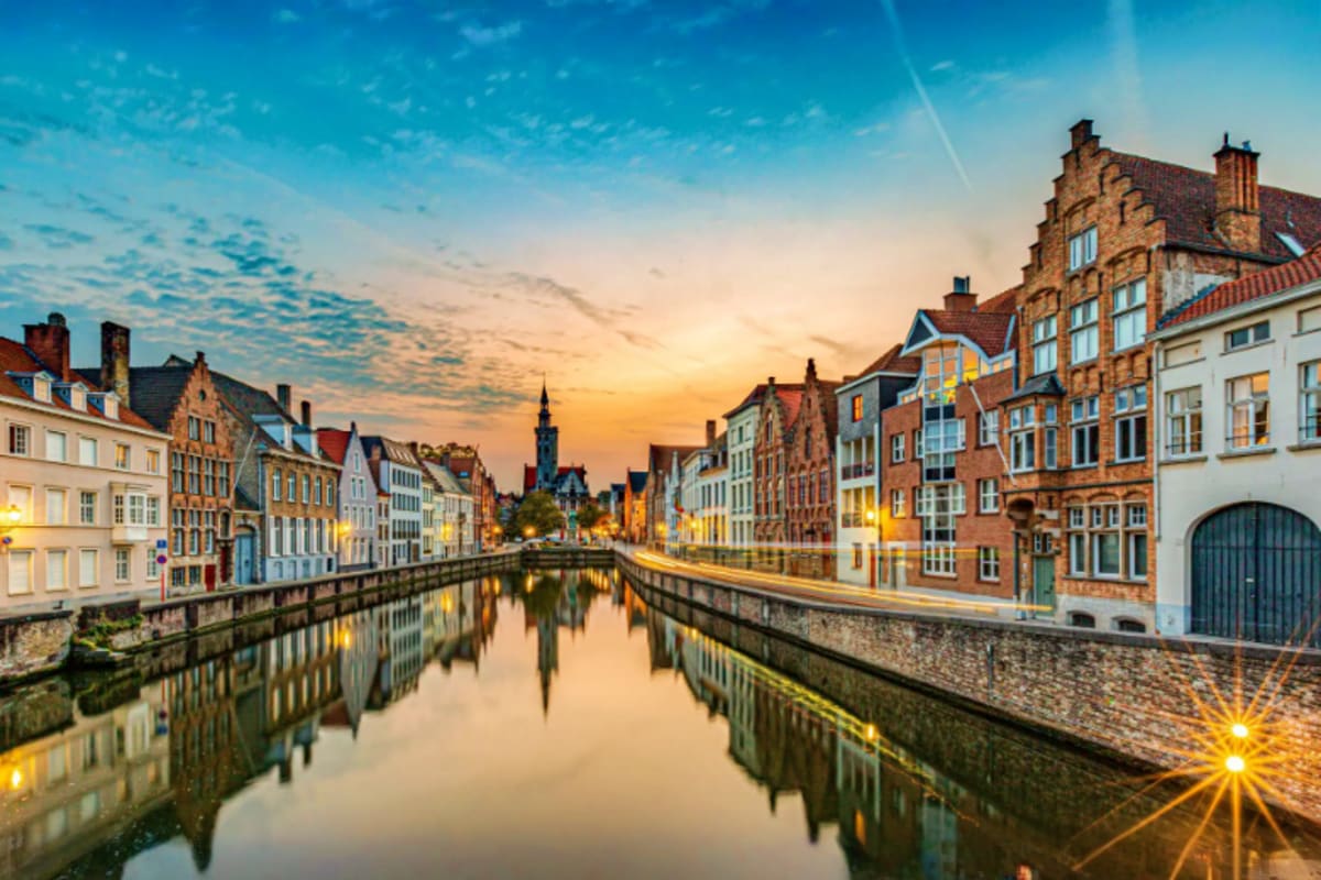 Historic European canal town at sunset with traditional brick buildings reflected in calm water, church spire in background