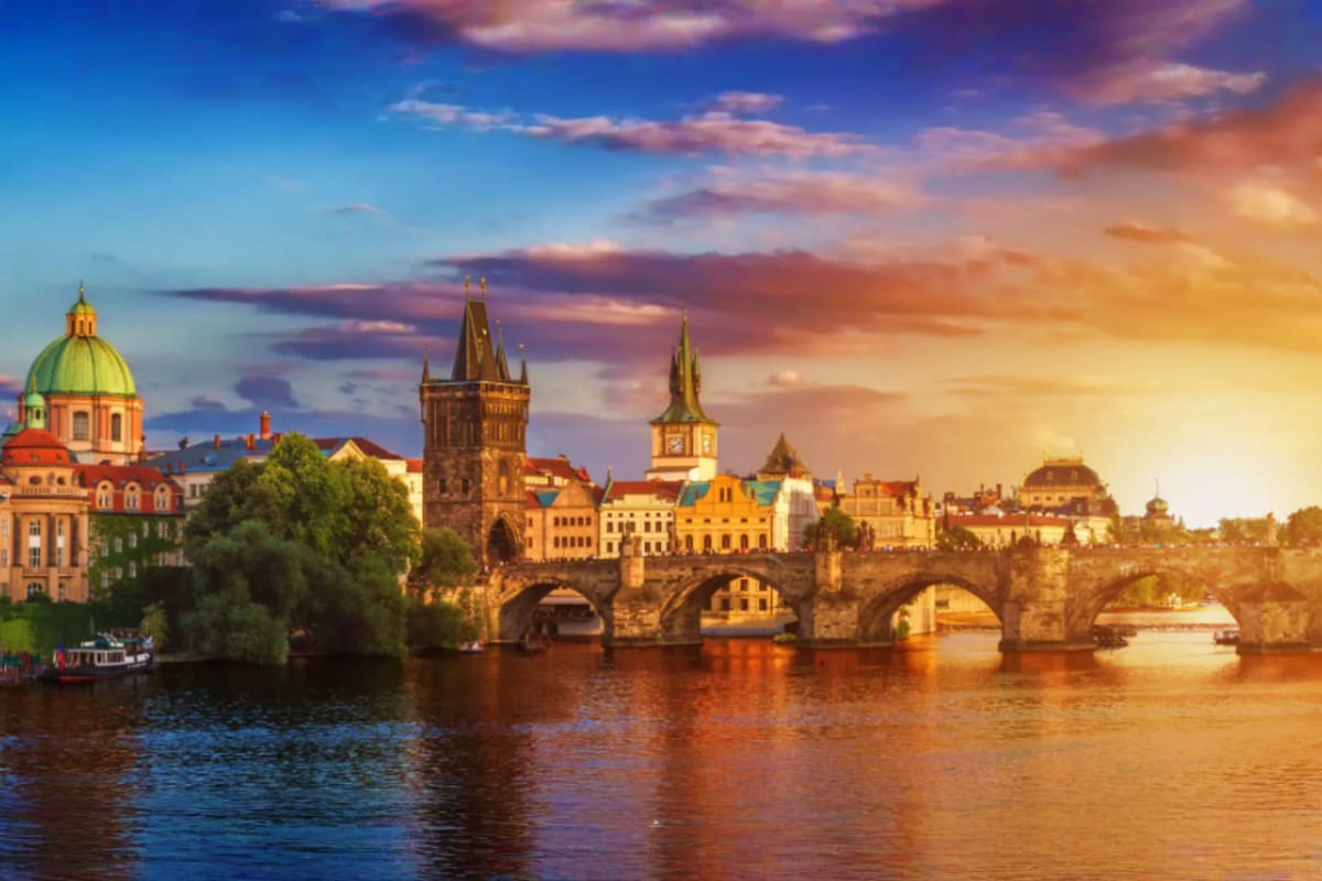 Prague cityscape at sunset with Charles Bridge, Vltava River, and historic towers reflecting in water