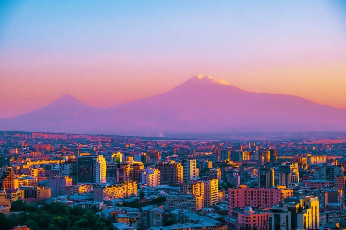Mount Ararat at sunrise with Yerevan cityscape, golden-lit buildings and purple sky