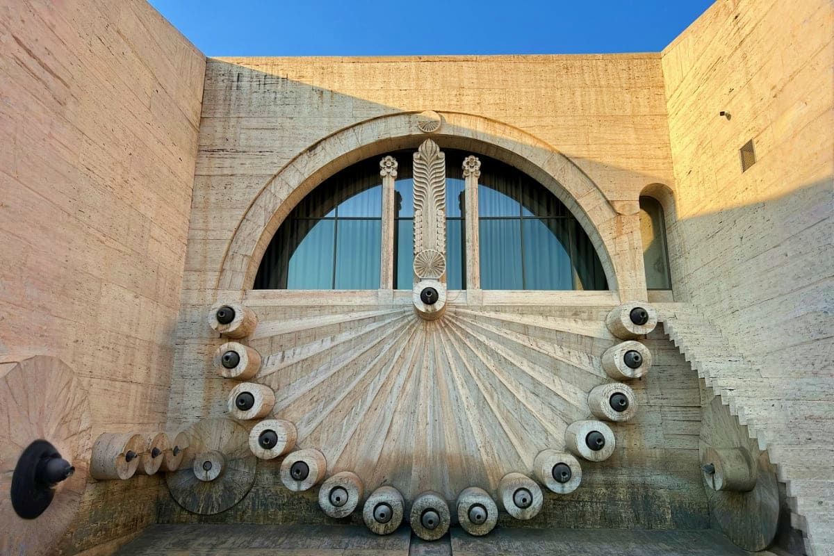 Art Deco sundial with ornamental spokes and spheres on stone wall beneath arched window at historic Armenian building