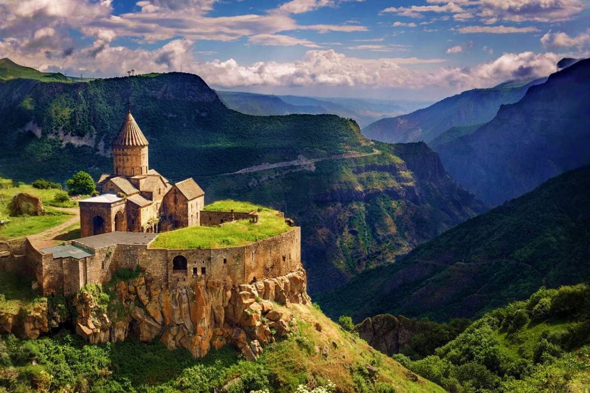 Tatev Monastery perched on a rocky cliff overlooking a lush green canyon valley in Armenia