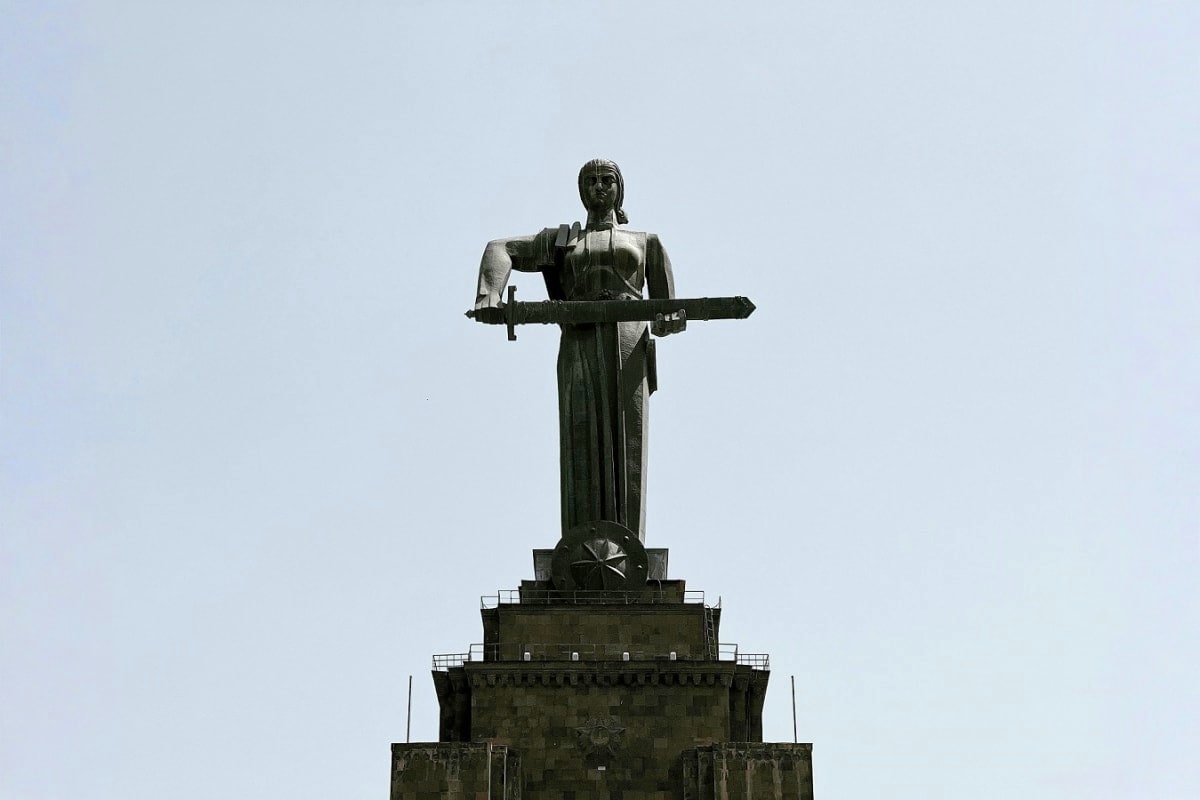 Monumental statue of female figure holding airplane on stone pedestal against clear sky, representing aviation heritage