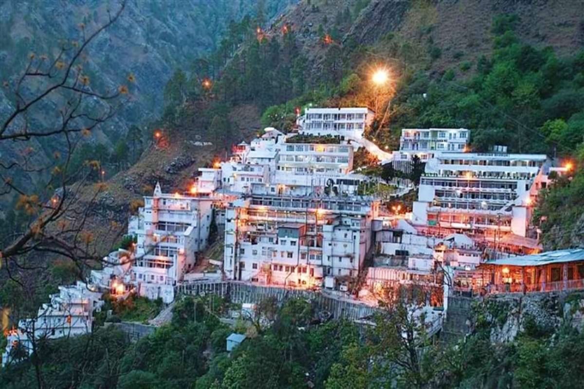 Vaishno Devi temple complex illuminated at dusk nestled in snow-capped Himalayan mountains surrounded by dense forest vegetat