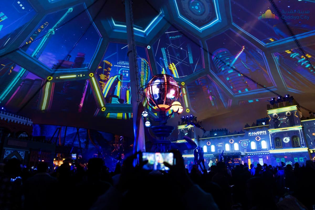 The Qiddiya Experience Futuristic neon-lit indoor venue at Qiddiya City with glowing blue and yellow geometric ceiling panels, illuminated spherical