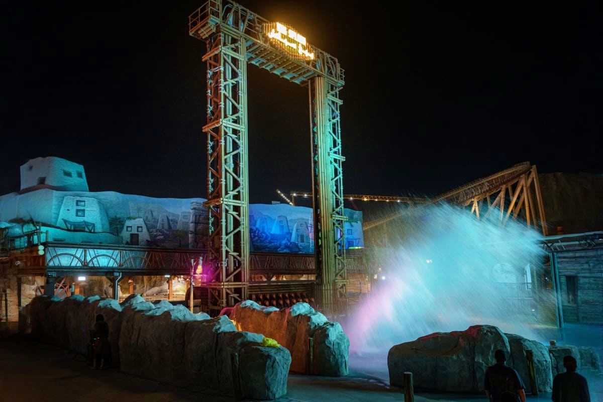 The Qiddiya Experience Night view of the Qiddiya Experience with illuminated industrial structures, artificial rock formations, and glowing water sp